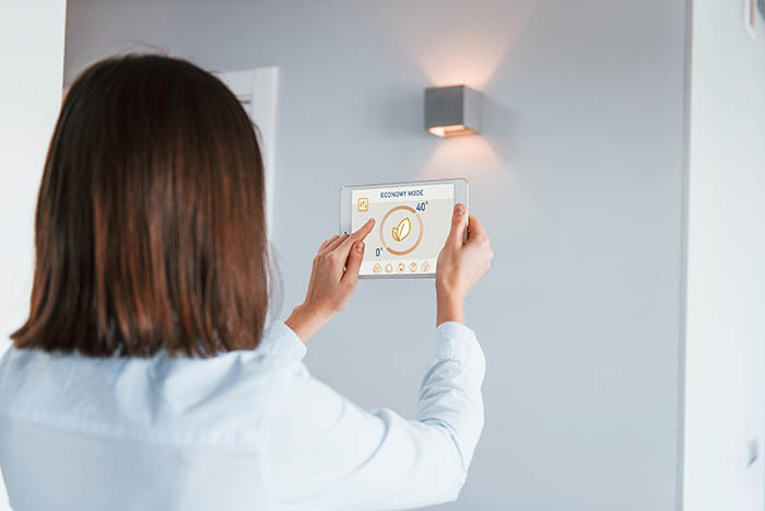 Rear view of woman that is indoors controlling smart home technology, using an underfloor heating thermostat.